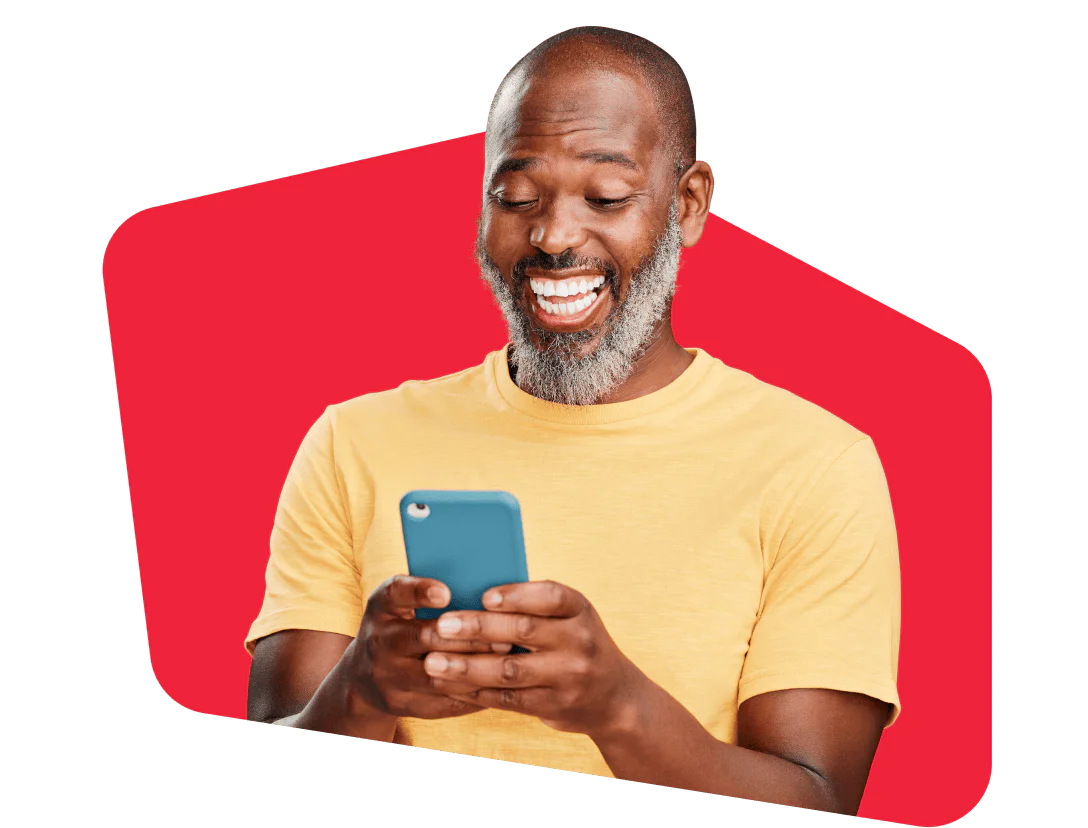 A smiling man with a beard using a smartphone against a red background.