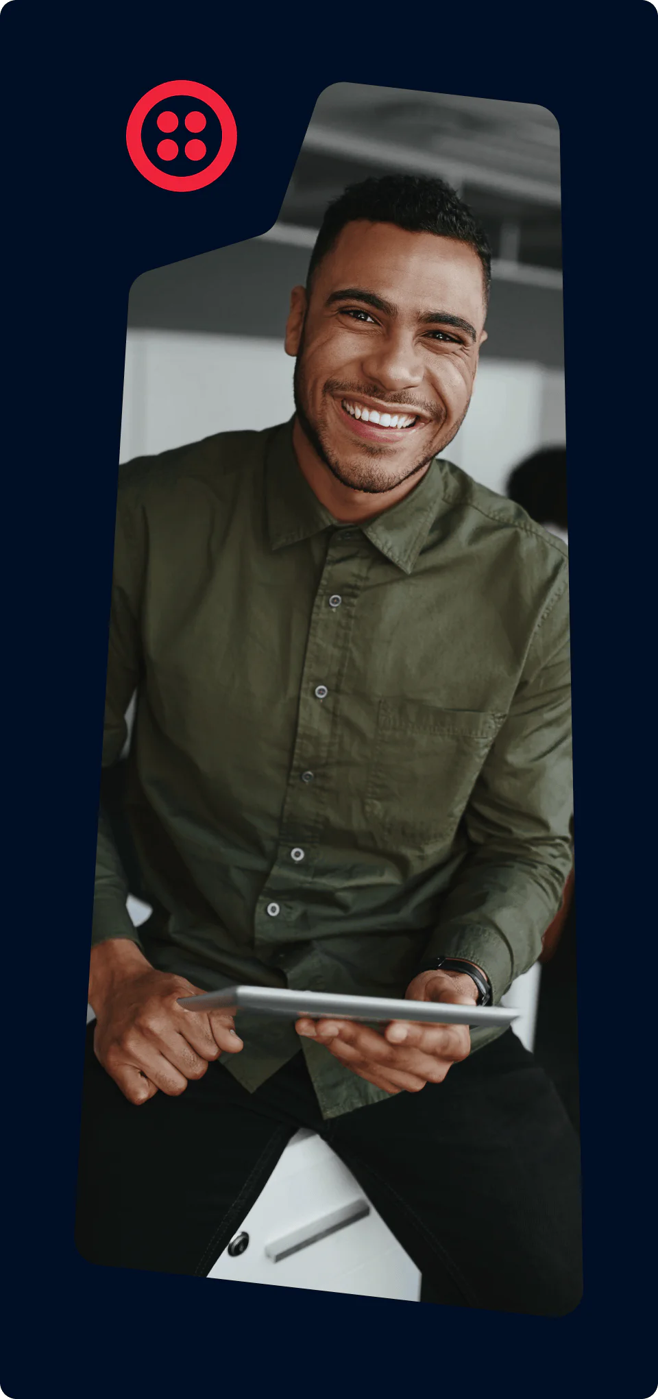 A man in a green shirt smiles while holding a tablet and sitting on a chair.