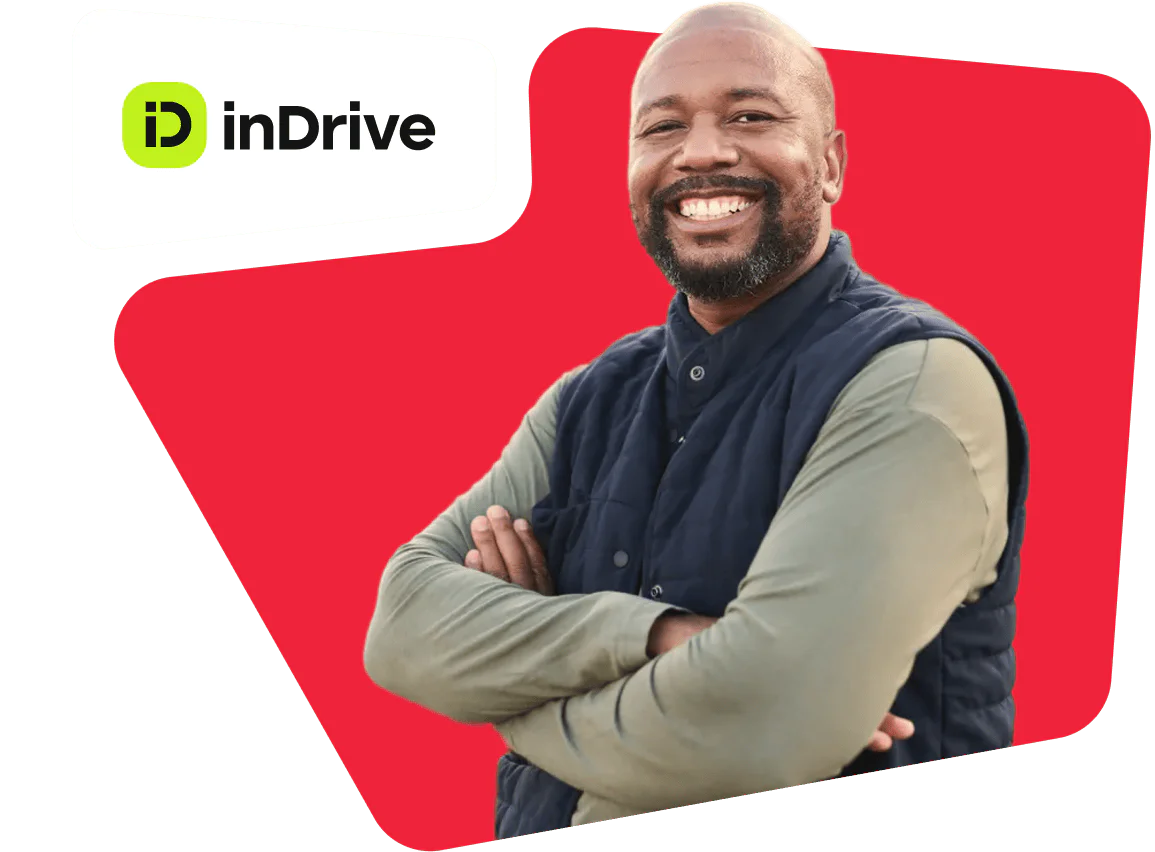 Smiling man with crossed arms in a vest and shirt, standing beside the inDrive logo on a red background.