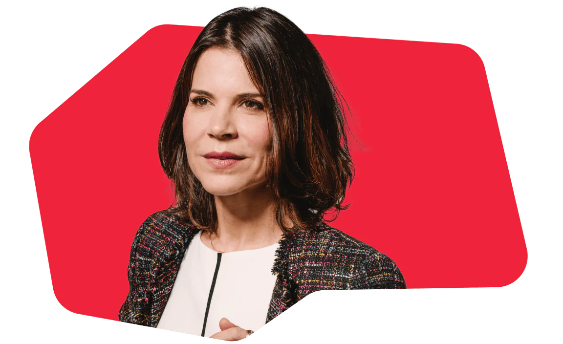 Woman with brown hair in a tweed jacket posing against a red background.