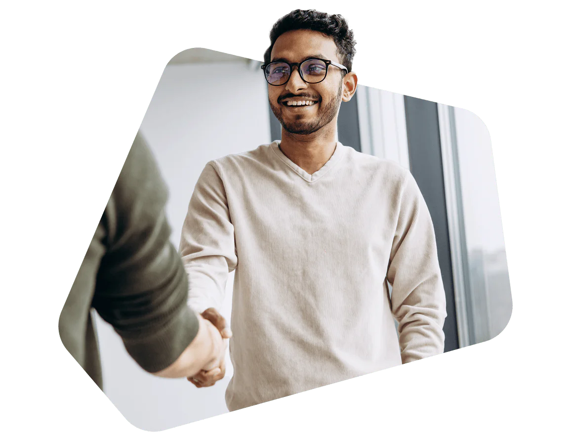 Smiling man in glasses shaking hands with another person in an office setting.