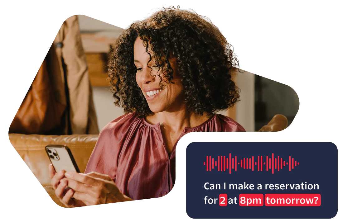 Woman smiling while using her phone with a voice assistant asking to make a reservation for 2 at 8pm.