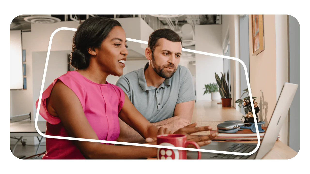 Two coworkers engrossed in a discussion, working together on a laptop in a modern, open office space.