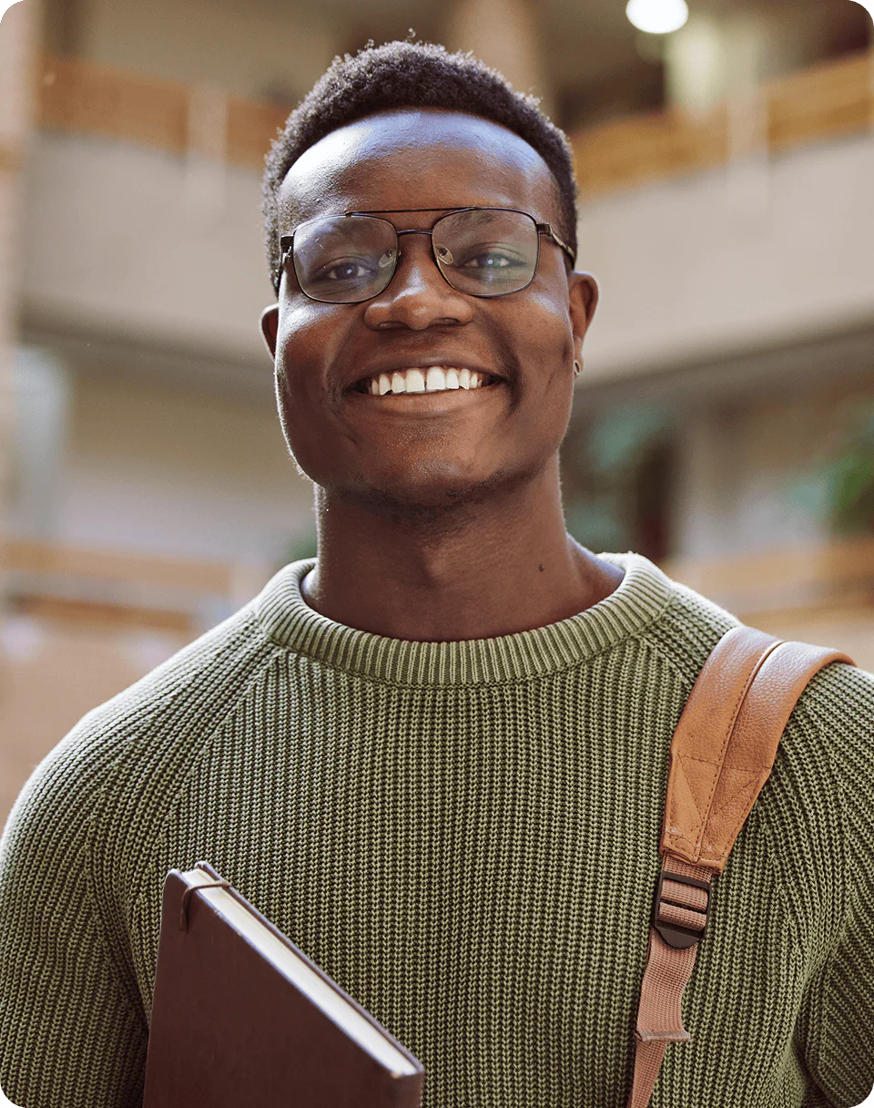 Young man with glasses and a green sweater, holding a book and smiling.