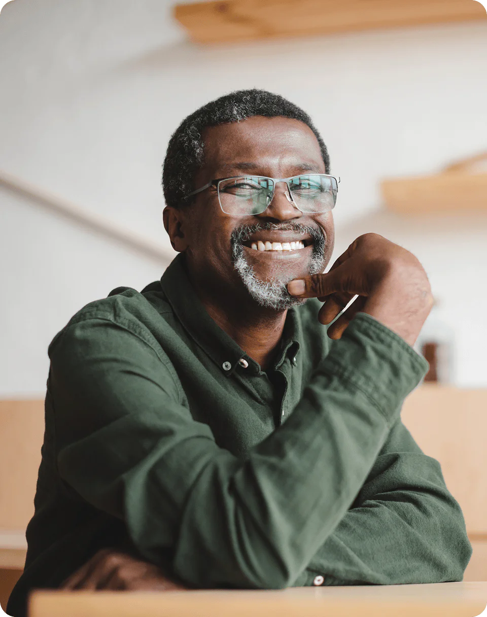 A man wearing glasses and a green shirt smiling with his arm resting on a table