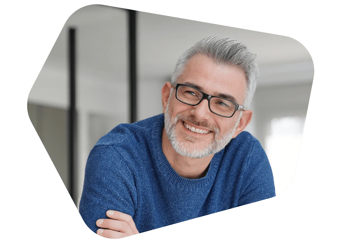 Smiling man with glasses in blue sweater indoors Man with grey hair and glasses wearing a blue sweater smiling indoors