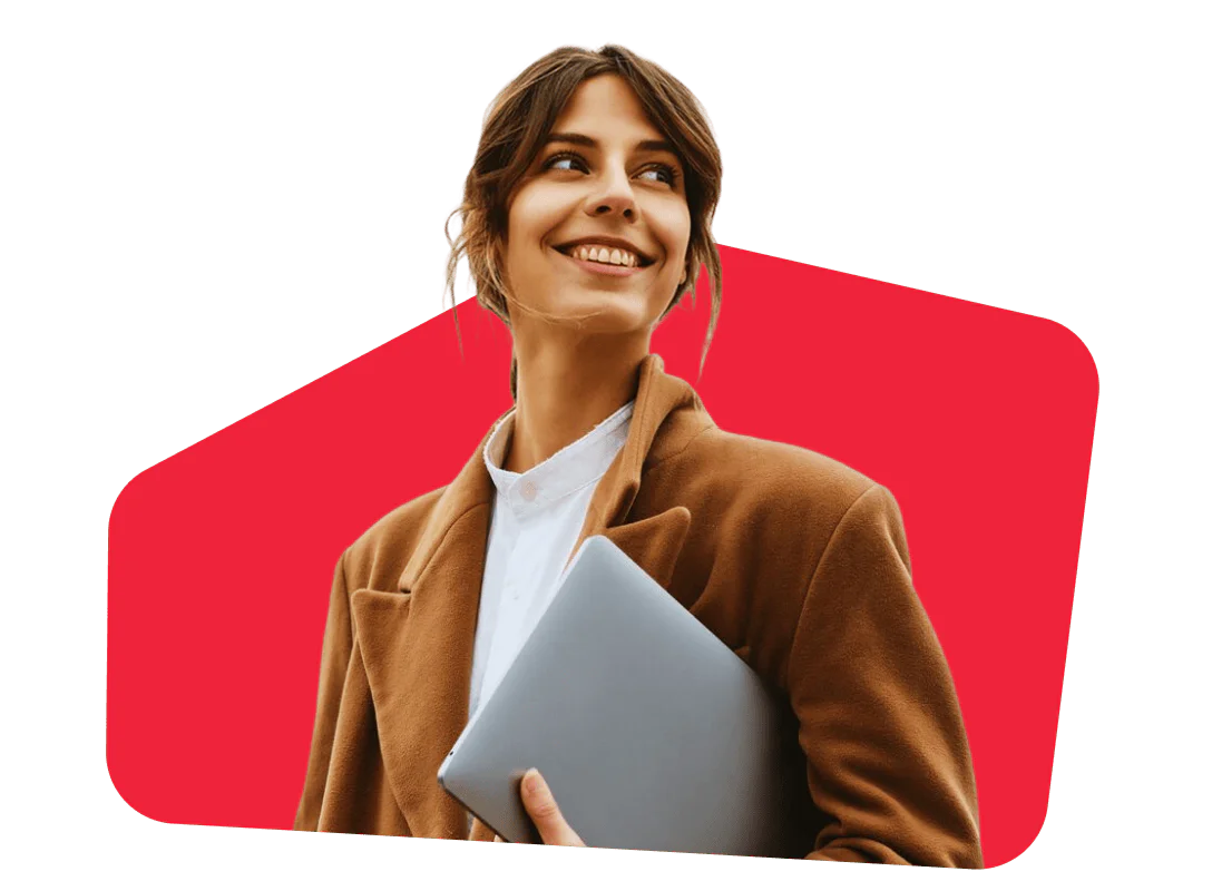 Woman in a brown coat smiling and holding a laptop against a red background