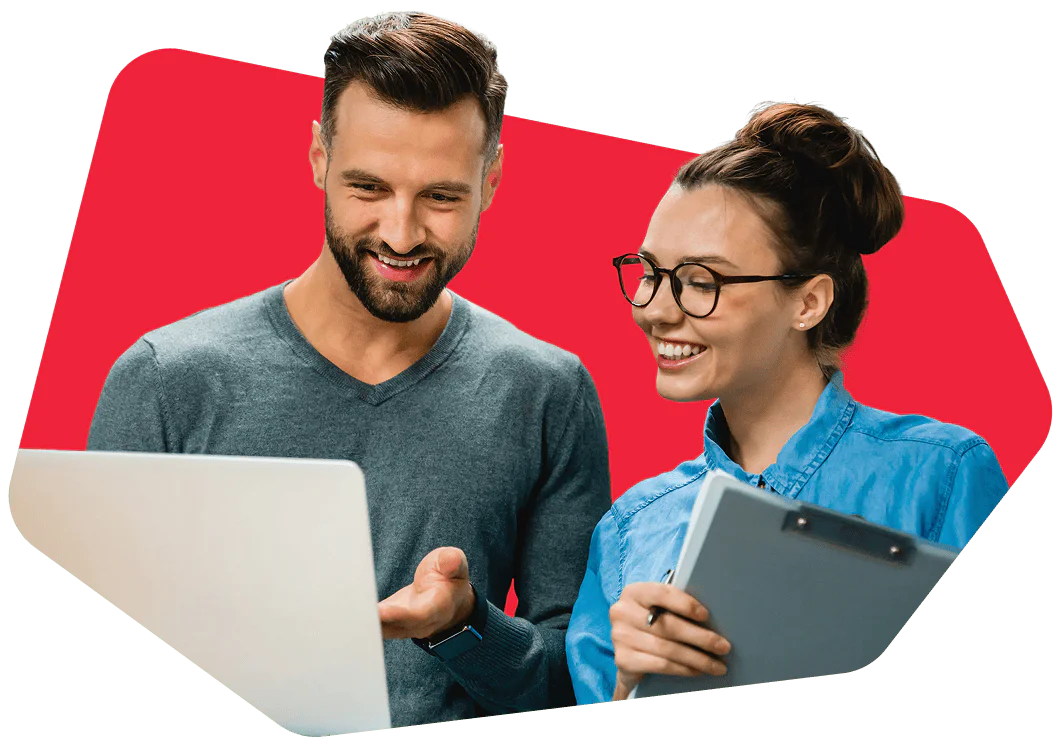 Man and woman smiling while looking at a laptop and a clipboard.