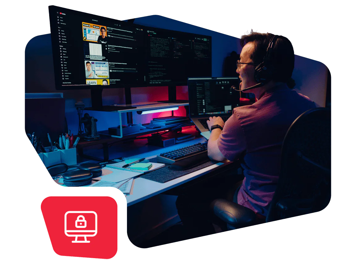 Man with a headset using dual monitors in a dark room with organized desk and lighting.
