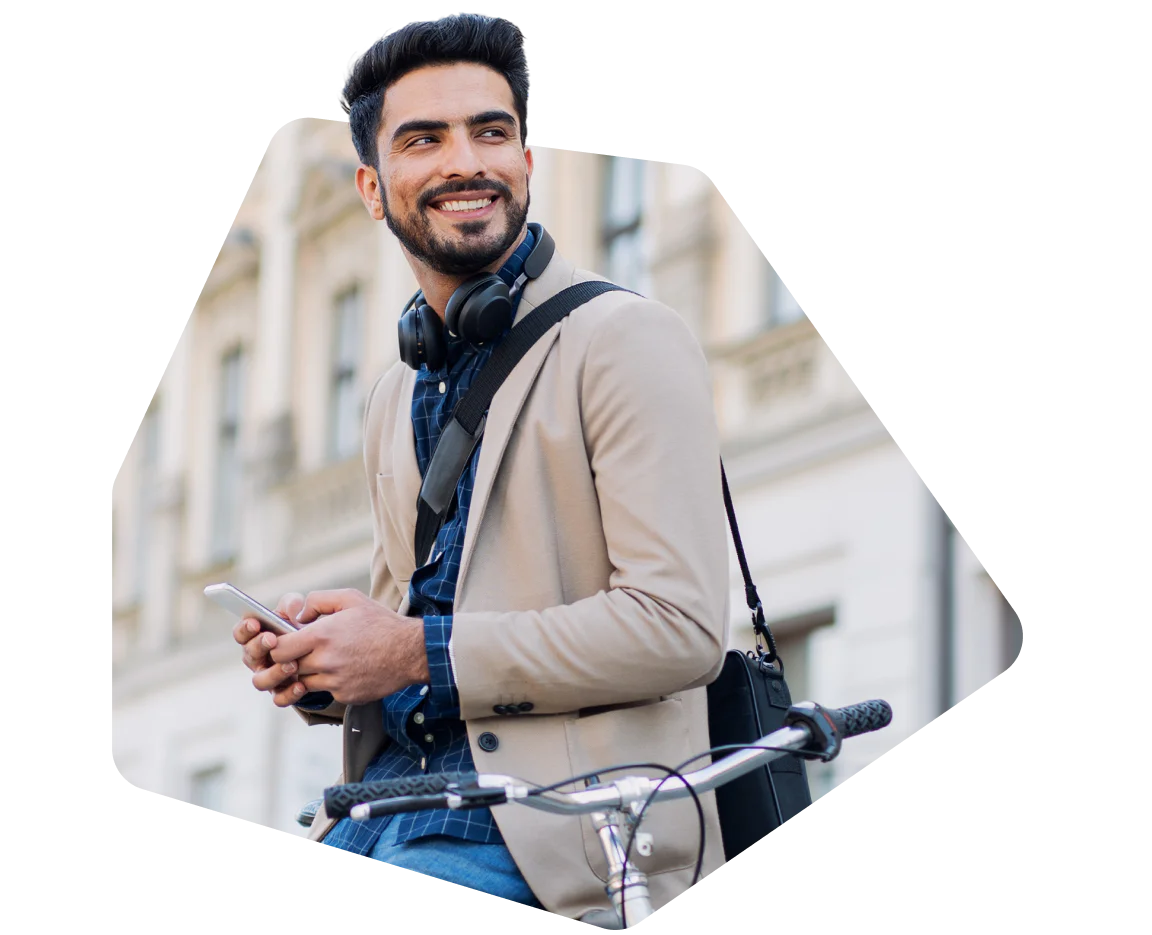 Smiling man wearing headphones and a beige blazer, holding a phone while resting on a bike.