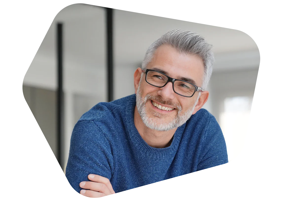 Man with grey hair and glasses wearing a blue sweater smiling indoors